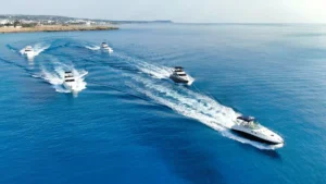 Aerial view of yachts with crisscrossing wakes in the blue waters near Ayia Napa, with the Cyprus coastline in the distance.