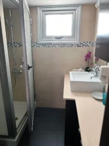 Modern Ayia Napa bathroom featuring a glass shower, beige tiles with mosaic border, and a frosted window for a bright, airy feel.