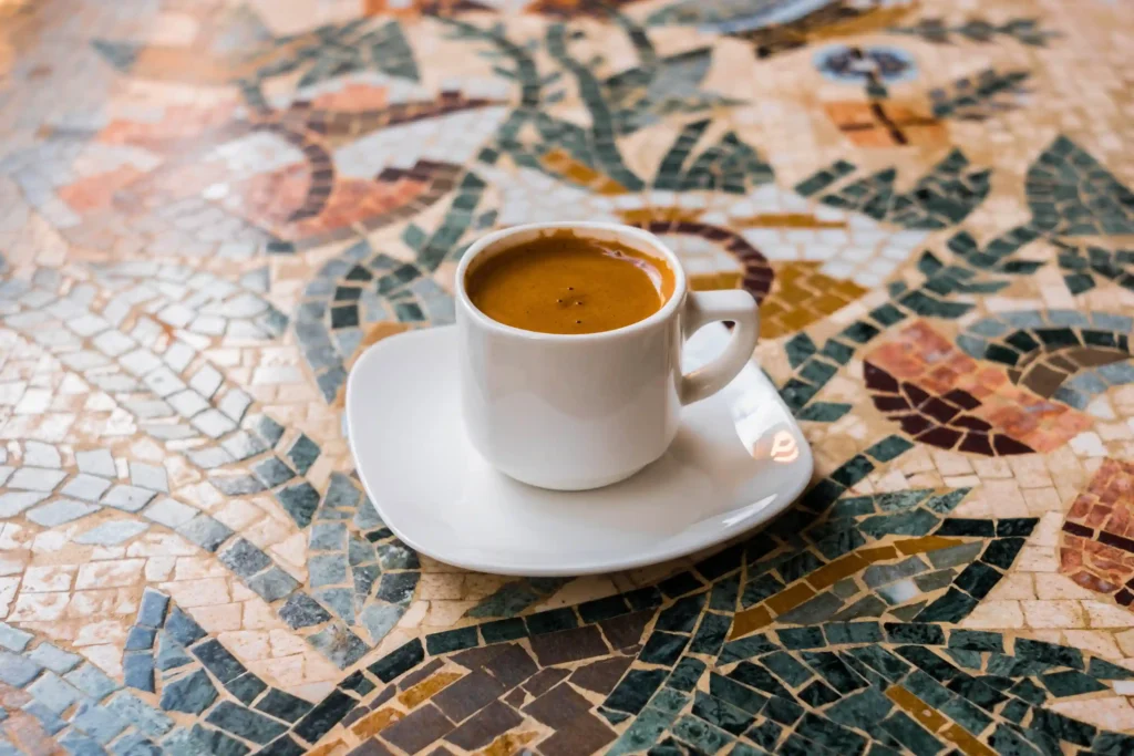 Traditional Cypriot coffee in a white cup on a saucer, placed on a colorful mosaic table, symbolizing local culture at a kafeneio in Cyprus.