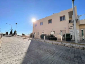 Modern residential building in Ayia Napa with a sunlit paved courtyard, spiral staircase, and lush greenery.