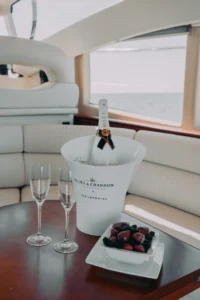 A luxury yacht interior featuring a bottle of Moët & Chandon champagne, two glasses, and fresh berries, with a view of the sea through the window.