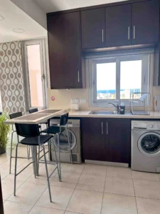 Chic open-floor kitchen with an island in Ayia Napa accommodation, showcasing seaside views through a kitchen window.