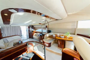 The luxurious cabin of a yacht with wood finishes and cream-colored seating, illuminated by natural light and interior lighting.