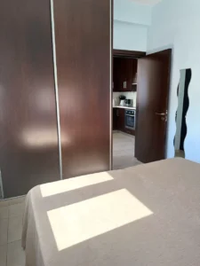 Cozy bedroom with natural sunlight and a view into the kitchen, part of a comfortable two-bedroom apartment in Ayia Napa, Cyprus.