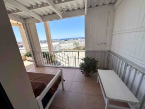 A shaded balcony with a bench and potted plant overlooking the scenic Ayia Napa skyline and sea.