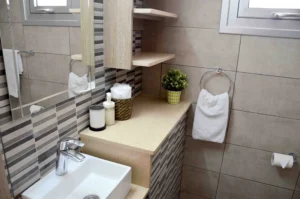 Modern bathroom with patterned tile work, wooden shelves, a white sink, and a small green plant, offering a serene spa-like environment.