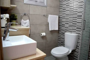 Modern bathroom with striped tile accent wall, rectangular basin, and wooden shelves, offering a refined and comfortable space in Ayia Napa.