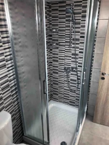 Modern shower enclosure with striped tiles, a sleek showerhead, and shelves in the bathroom of an Ayia Napa apartment.