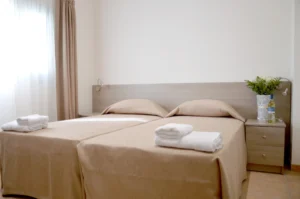 Twin beds with beige linens in a bright, minimalistic Ayia Napa bedroom, adorned with a small vase of fresh flowers.