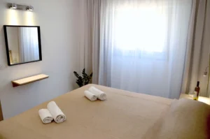 Serene bedroom with natural light, sheer curtains, a mirror, and soft bedding in a modern stylish Ayia Napa apartment.