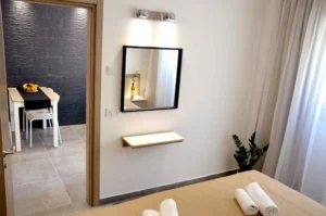 Modern bedroom with a mirror reflecting the dining area's black textured wall, a glimpse of the stylish interior of an Ayia Napa apartment.