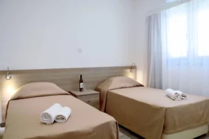 Bright and minimalist twin bedroom with two single beds, soft lighting, and sheer curtains in a stylish Ayia Napa apartment.