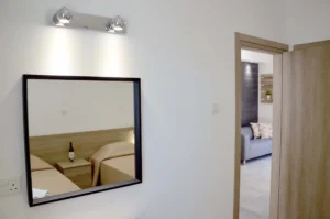 Modern bedroom with a reflection in the mirror showing the entrance to the living area, featuring a sleek design and inviting ambiance in an Ayia Napa apartment.