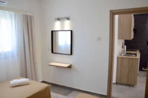 Simple and elegant bedroom with natural light and a view through the doorway to the apartment's kitchenette in Ayia Napa.