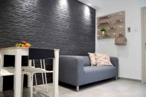 Elegant and modern living room in Ayia Napa apartment featuring a black textured wall, gray sofa, white dining furniture, and a bowl of fruit on the table.