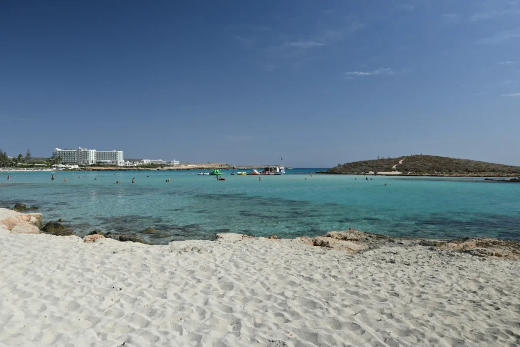 Visitors enjoying water sports in the turquoise waters of Nissi Beach with a view of the sandy shore and resort buildings in Ayia Napa, Cyprus.