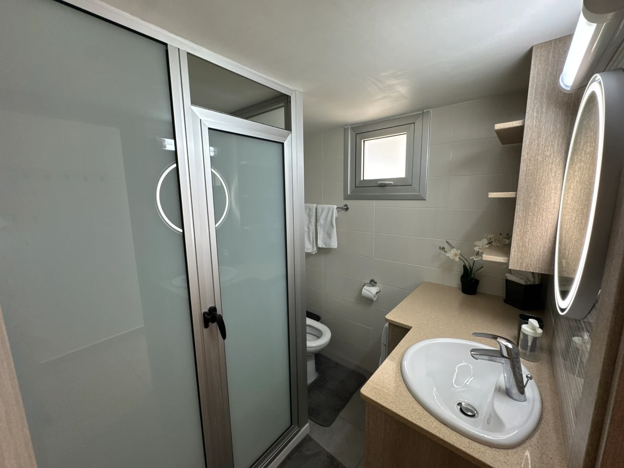 Modern bathroom with a shower, sink, and illuminated mirror in the Charming Central Apartment with Sea View Balcony, Ayia Napa, Cyprus.