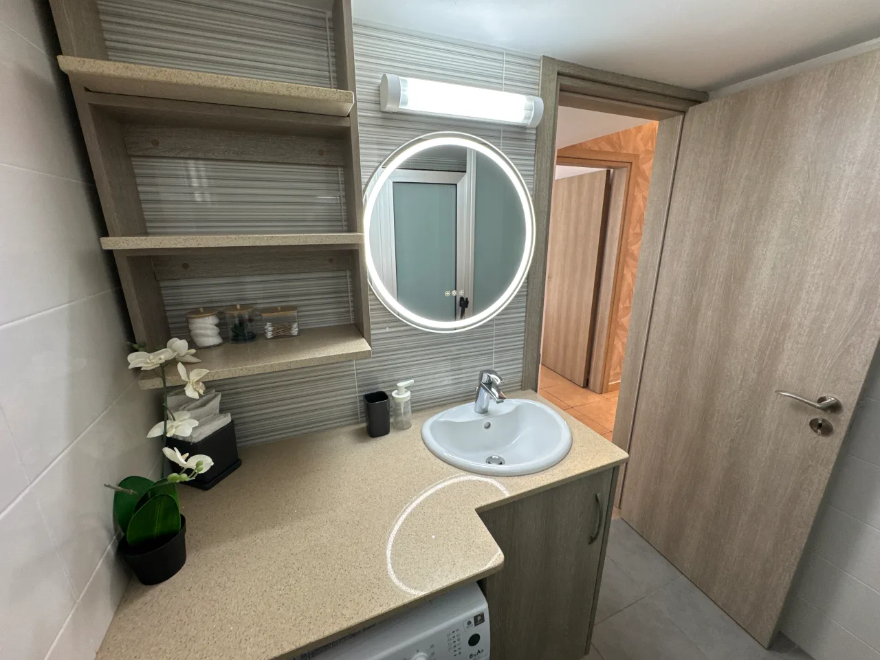 Modern bathroom with a sink, illuminated mirror, and shelves in the Charming Central Apartment with Sea View Balcony, Ayia Napa, Cyprus.