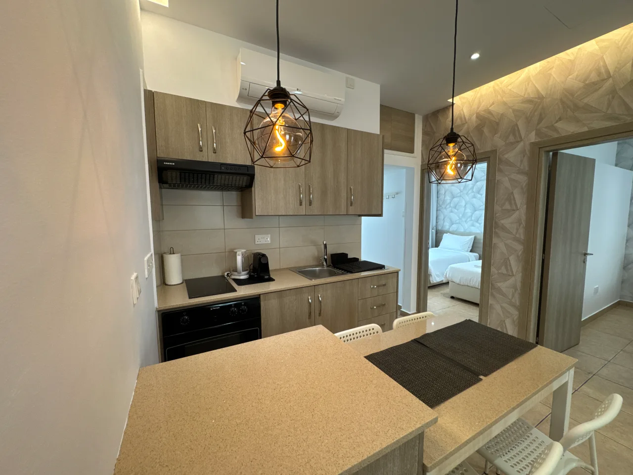 Well-equipped kitchen and dining table with chairs in the Charming Central Apartment in Ayia Napa, Cyprus, with a view into a bedroom.