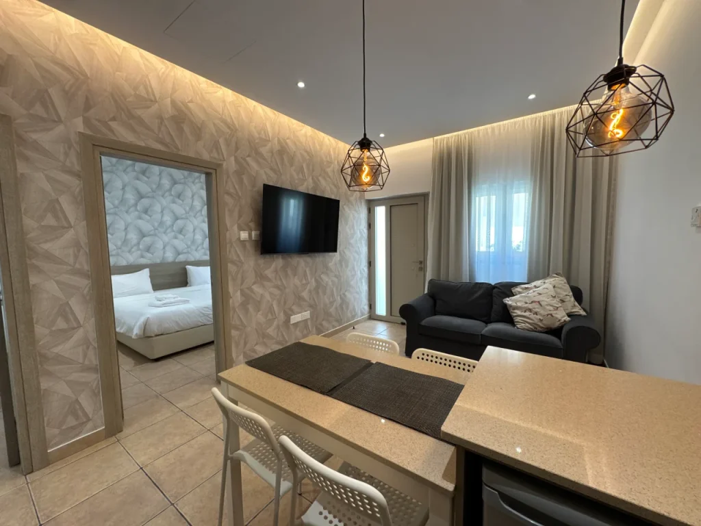 Modern living area with a sofa, TV, dining counter, and a view into a bedroom at our holiday rental in Ayia Napa, Cyprus.