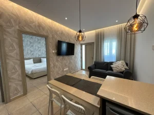 Modern living area with a sofa, TV, dining counter, and a view into a bedroom at our holiday rental in Ayia Napa, Cyprus.